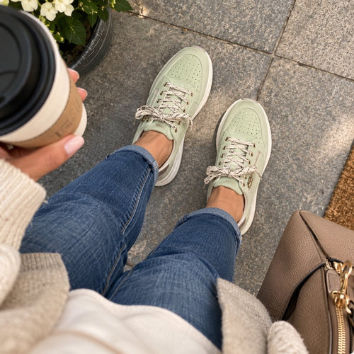 Soft sage green sneakers with lace-up detail, styled with denim